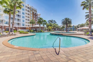 Una piscina envoltada de palmeres i un edifici d'hotel de diversos pisos.