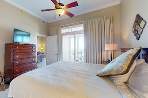 A bedroom with a bed, a dresser, a ceiling fan, a TV, a balcony, and curtains. - Bayfront condo w/ amazing views, shared hot tub & community pool (Panama City Beach)