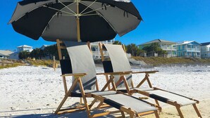 Ein Strand mit Holzliegen und einem großen Sonnenschirm.