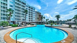 En stor inomhuspool med ett trädäck runt om, en hotellbyggnad i bakgrunden och palmer.
