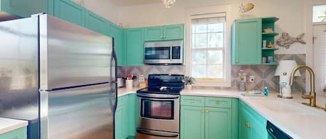 A kitchen with teal cabinets, stainless steel appliances, a chandelier, and a window with a view.