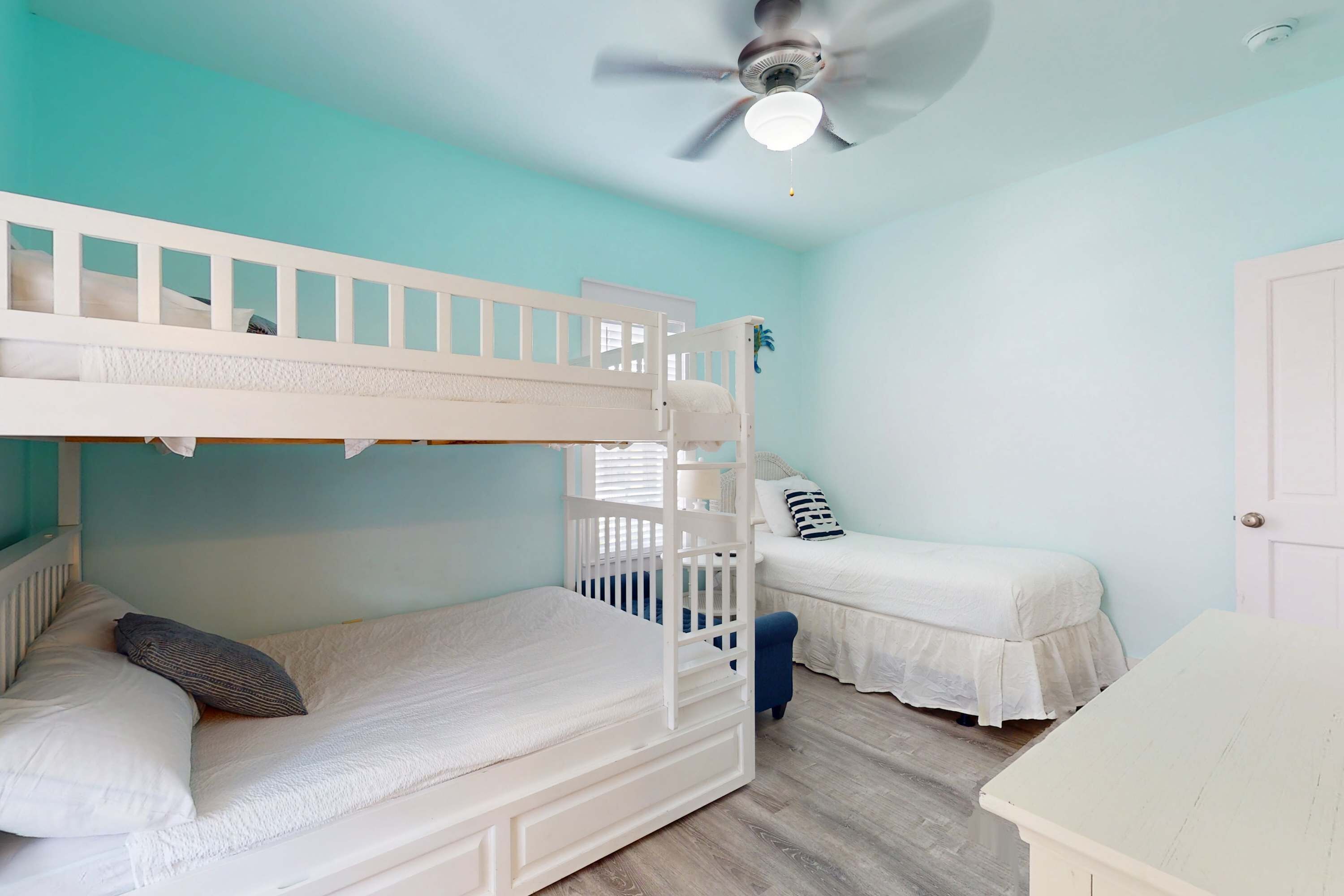 Ein Schlafzimmer mit Etagenbetten, Deckenventilator, kleinem Schreibtisch und Tür.