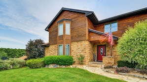A two-story house with a stone foundation, a red door, and a flag. - 7,000 Sq Ft! Private Rapid City Estate w/ Pool (Rapid City)