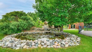 A pond with a stone border, surrounded by lush greenery and a building in the background. - 7,000 Sq Ft! Private Rapid City Estate w/ Pool (Rapid City)