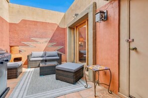 Une terrasse extérieure accueillante, avec des meubles en osier, une petite table et un barbecue.