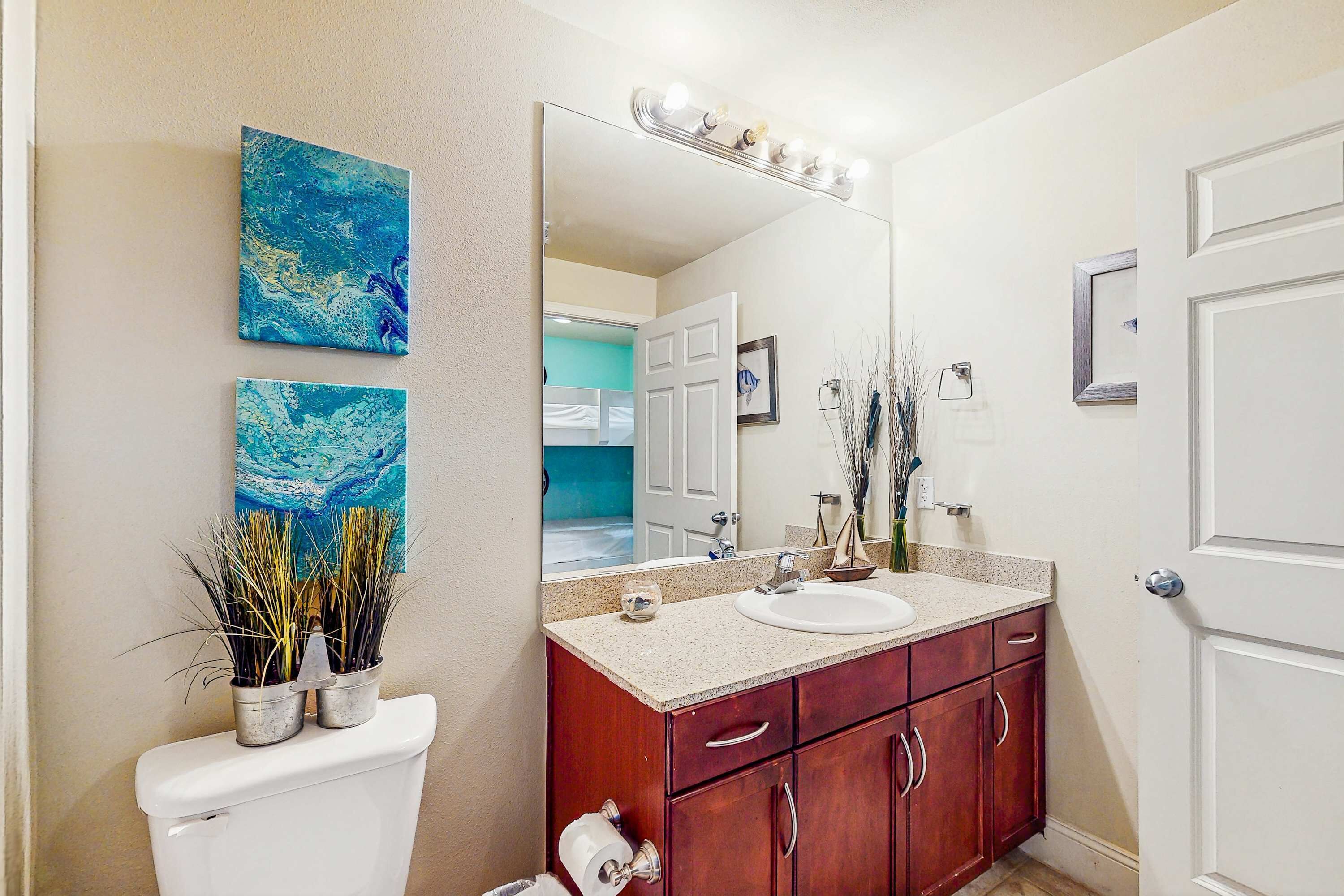 Une salle de bain avec des toilettes blanches, un meuble-lavabo et deux tableaux abstraits bleus accrochés au mur.
