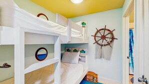 Une chambre avec des lits superposés décorée sur le thème de la marine, avec notamment un décor représentant une roue de navire et des œuvres d’art encadrées accrochées au mur.