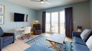 Ein Wohnzimmer mit Flachbildfernseher, Deckenventilator, Sofa, Couchtisch, Schreibtisch und Stuhl.