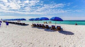Ein Strand mit Reihen von Liegestühlen und Sonnenschirmen, ein klarer Himmel und das Meer im Hintergrund.