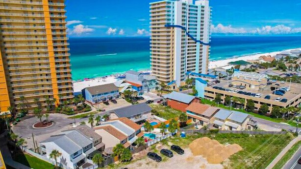 Un hotel costero con varios edificios altos, una playa y un estacionamiento.