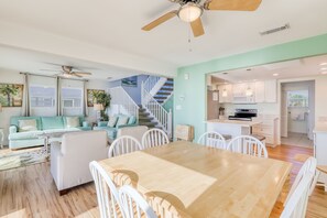 A spacious living area with a wooden dining table, white chairs, a teal sofa, and a staircase leading to a kitchen area. - Beachfront home with coastal views & beach access - dog-friendly (Cape San Blas)