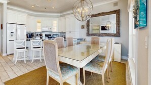 A modern kitchen with white cabinetry, a glass-top dining table, wicker chairs, and a decorative mirror. - Gorgeous gulf-front condo, shared outdoor pool  - beach service included (Santa Rosa Beach)