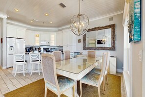 A modern kitchen with white cabinetry, a glass-top dining table, wicker chairs, and a decorative mirror. - Gorgeous gulf-front condo, shared outdoor pool  - beach service included (Santa Rosa Beach)