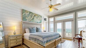 A bedroom with a large bed, a ceiling fan, a painting, and a view of the ocean through the window. - Gorgeous gulf-front condo, shared outdoor pool  - beach service included (Santa Rosa Beach)