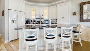 A modern kitchen with white cabinetry, a central island with bar stools, and a large mirror above the island. - Gorgeous gulf-front condo, shared outdoor pool  - beach service included (Santa Rosa Beach)