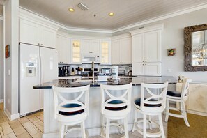 A modern kitchen with white cabinetry, a central island with bar stools, and a large mirror above the island. - Gorgeous gulf-front condo, shared outdoor pool  - beach service included (Santa Rosa Beach)