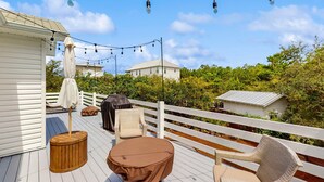 Una terraza con mobiliario exterior, luces colgantes y una valla blanca.