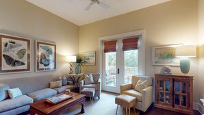 A living room with a sofa, armchairs, a coffee table, and a cabinet. There are framed pictures on the wall, a lamp, and a plant.