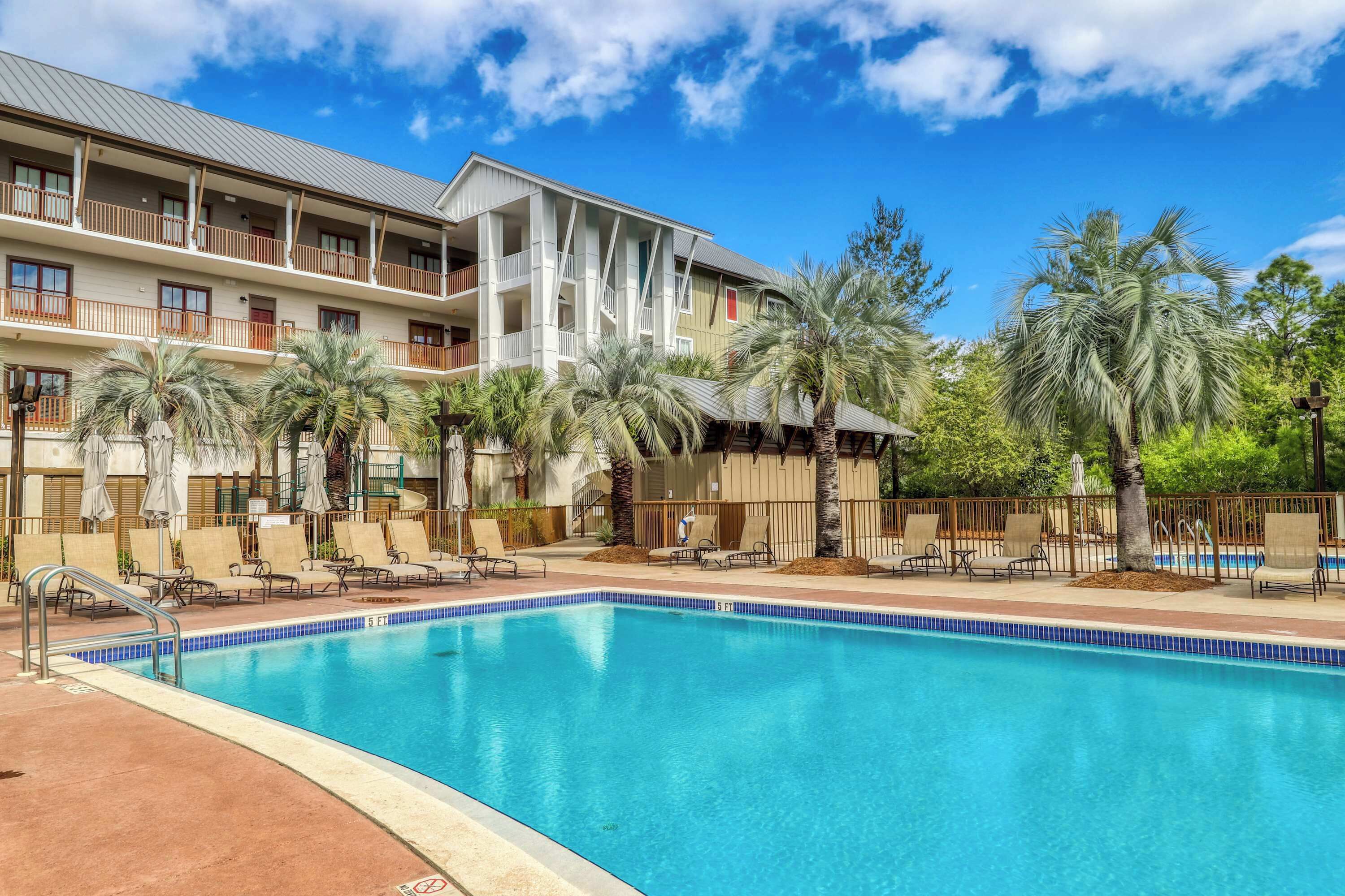 A hotel with a swimming pool, palm trees, and a multi-story building with balconies.