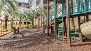 A playground area with a slide, climbing structures, and palm trees.