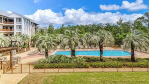 A hotel with a pool surrounded by palm trees, a covered patio area, and a fenced walkway.