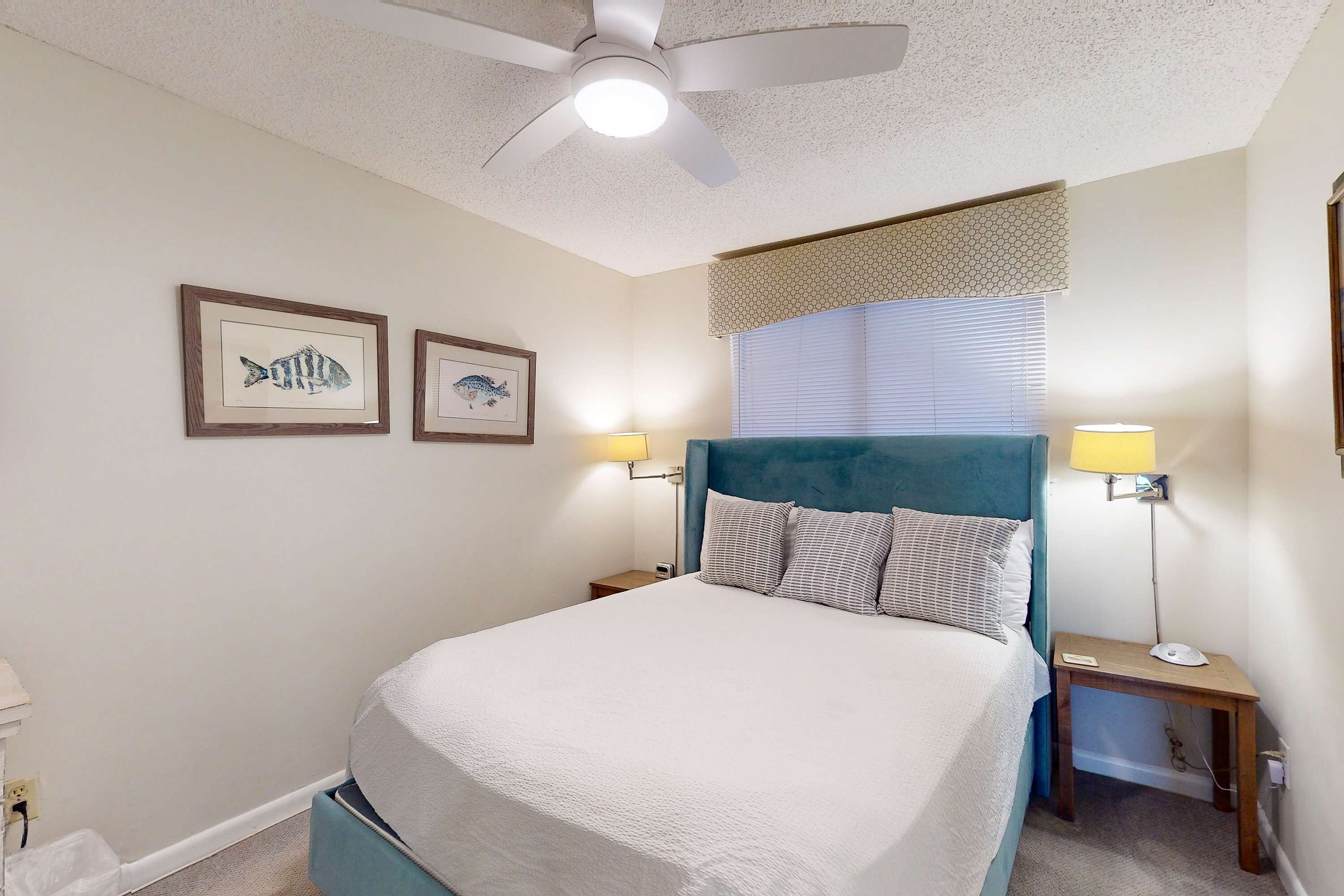 Et soveværelse med seng, loftventilator, to væglamper og to billeder af fisk.