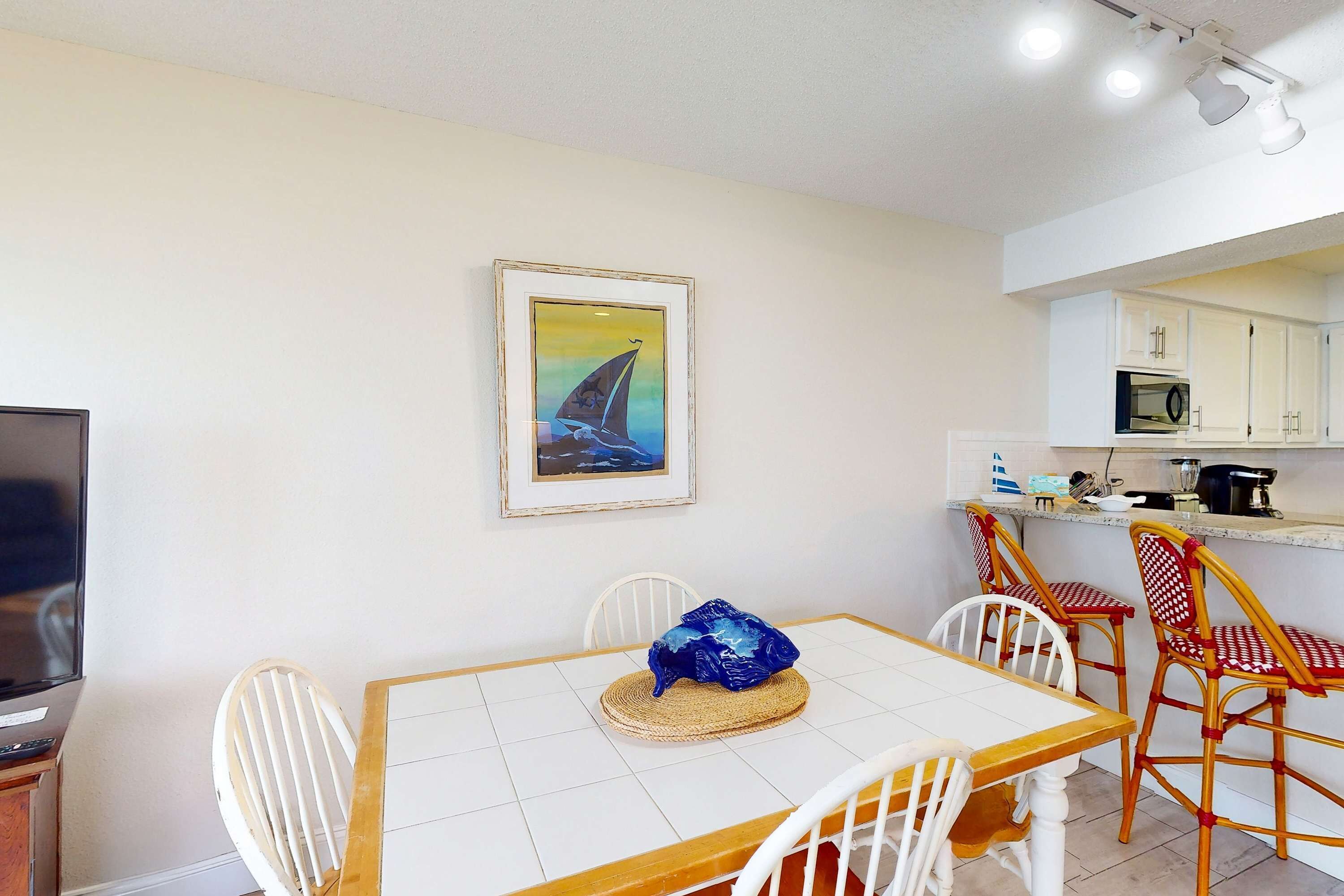 A dining area with a table, chairs, a television, and a kitchen in the background.