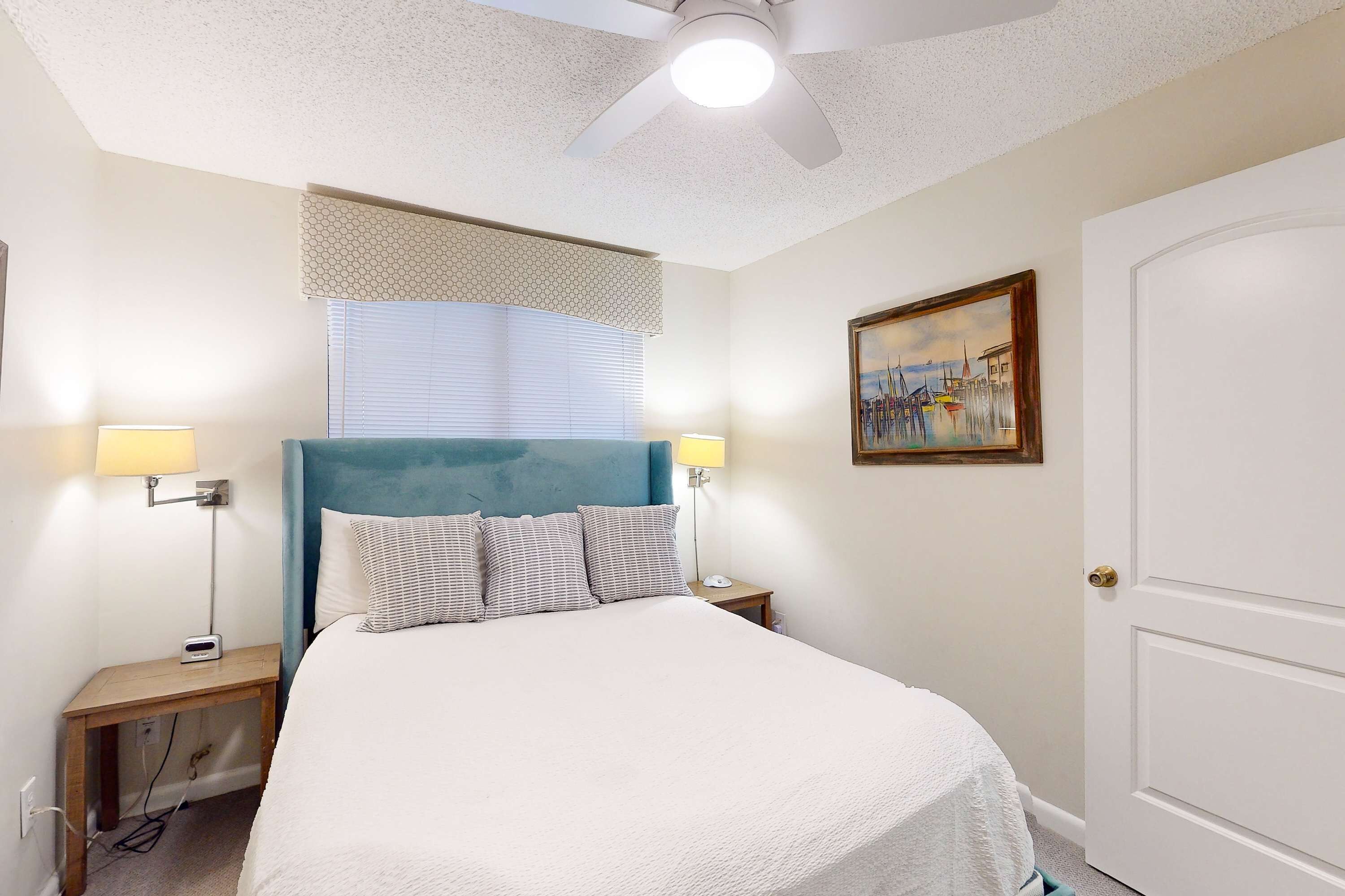A bedroom with a bed, two bedside tables, a ceiling fan, a window with blinds, and a door.