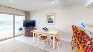 Un comedor con una mesa y sillas de madera, un televisor y vistas al océano a través de amplios ventanales.