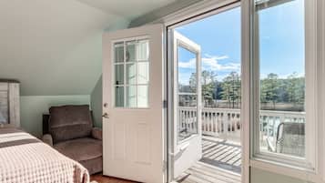 A bedroom with a large window, a door, a chair, and a bed.