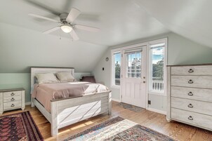 Quarto com cama, penteoudeiro, ventoinha no teto e porta que dá para o exterior.