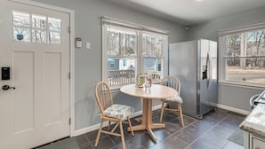 A kitchen with a round wooden table, two chairs, a refrigerator, and large windows. - Northern Neck Nature Retreat w/ Boat Ramp & Dock! (Heathsville)