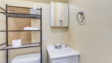 A bathroom with a white toilet, a sink with a mirror above it, and a metal shelf unit with towels and a roll of toilet paper.