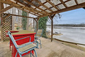 Une terrasse couverte, dotée d’une table et de chaises, qui offre une vue sur un lac paisible.