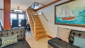Un salon avec un escalier, un tableau représentant un voilier et deux canapés avec des coussins.