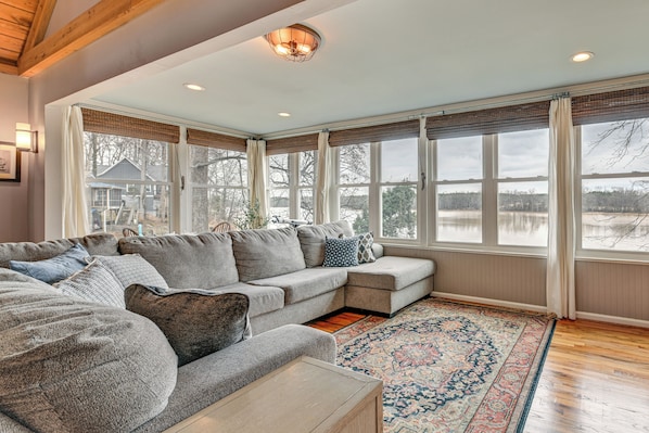 A cozy living room with a sectional sofa, a wooden coffee table, and a large window with a view of a lake.