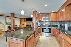A spacious kitchen with wooden cabinets, granite countertops, stainless steel appliances, and pendant lighting.