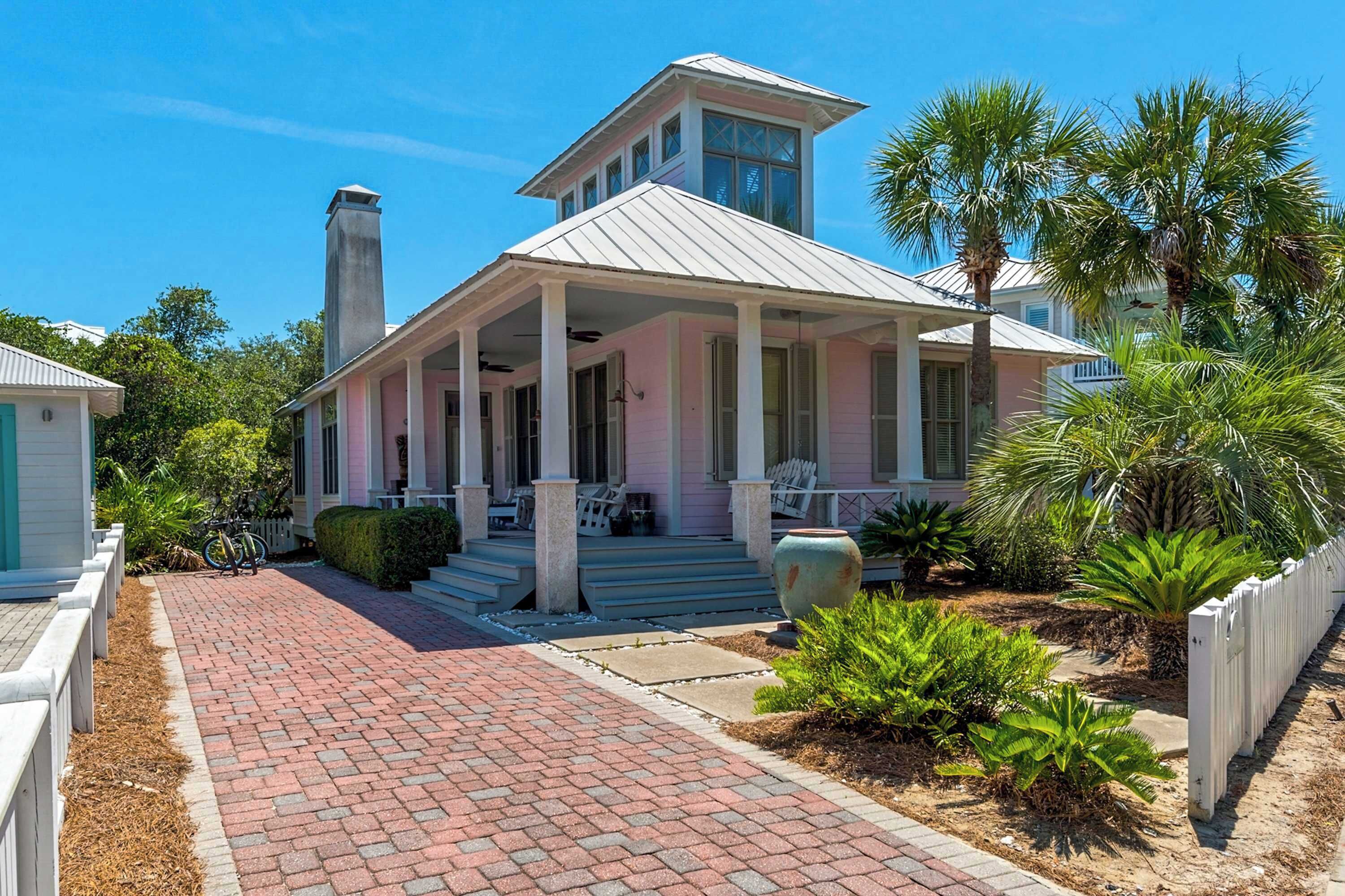 A two-story house with a covered porch, a chimney, and a garden with palm trees.