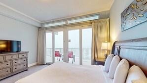 Hotellihuone, jossa on suuri sänky, televisio, tuoleilla varustettu parveke ja näkymä ulos.