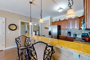A kitchen with granite countertops, wooden cabinets, and a stainless steel refrigerator. - High-rise condo with pool, hot tub, central AC, & free WiFi (Panama City Beach)
