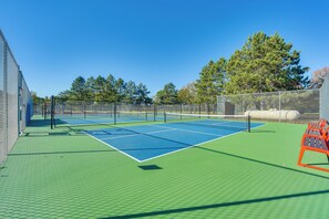 An outdoor tennis court with a green surface, surrounded by a fence, and trees in the background. - Fish, Swim, Play: 'voyagers' Family Cabin w/ Yard (Danbury)