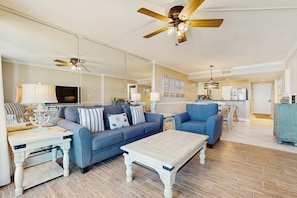 A spacious living room with a sofa, coffee table, and a television. There is a kitchen area in the background. - Gorgeous beach view condo, Shared pool and Beach access (Panama City Beach)