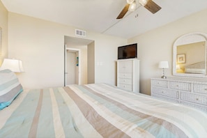 A bedroom with a bed, a dresser, a television, and a ceiling fan. - Gorgeous beach view condo, Shared pool and Beach access (Panama City Beach)