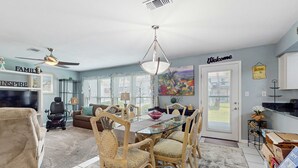 A living room with a glass-top dining table, wicker chairs, a ceiling fan, and a 'Welcome' sign on the door. - Coastal Townhouse with WiFi, Central AC, and Shared Pool (Navarre)
