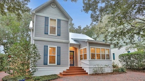 A two-story house with a front entrance, a brick driveway, and a small garden area. - Centrally located home with enclosed yard, grill, high ceilings, smart TVs, & AC (Santa Rosa Beach)