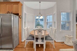 A dining area with a round table, white chairs, and a stainless steel refrigerator. - Centrally located home with enclosed yard, grill, high ceilings, smart TVs, & AC (Santa Rosa Beach)