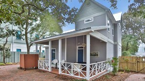 A two-story house with a covered porch, a fenced yard, and a brick pathway. - Centrally located home with enclosed yard, grill, high ceilings, smart TVs, & AC (Santa Rosa Beach)