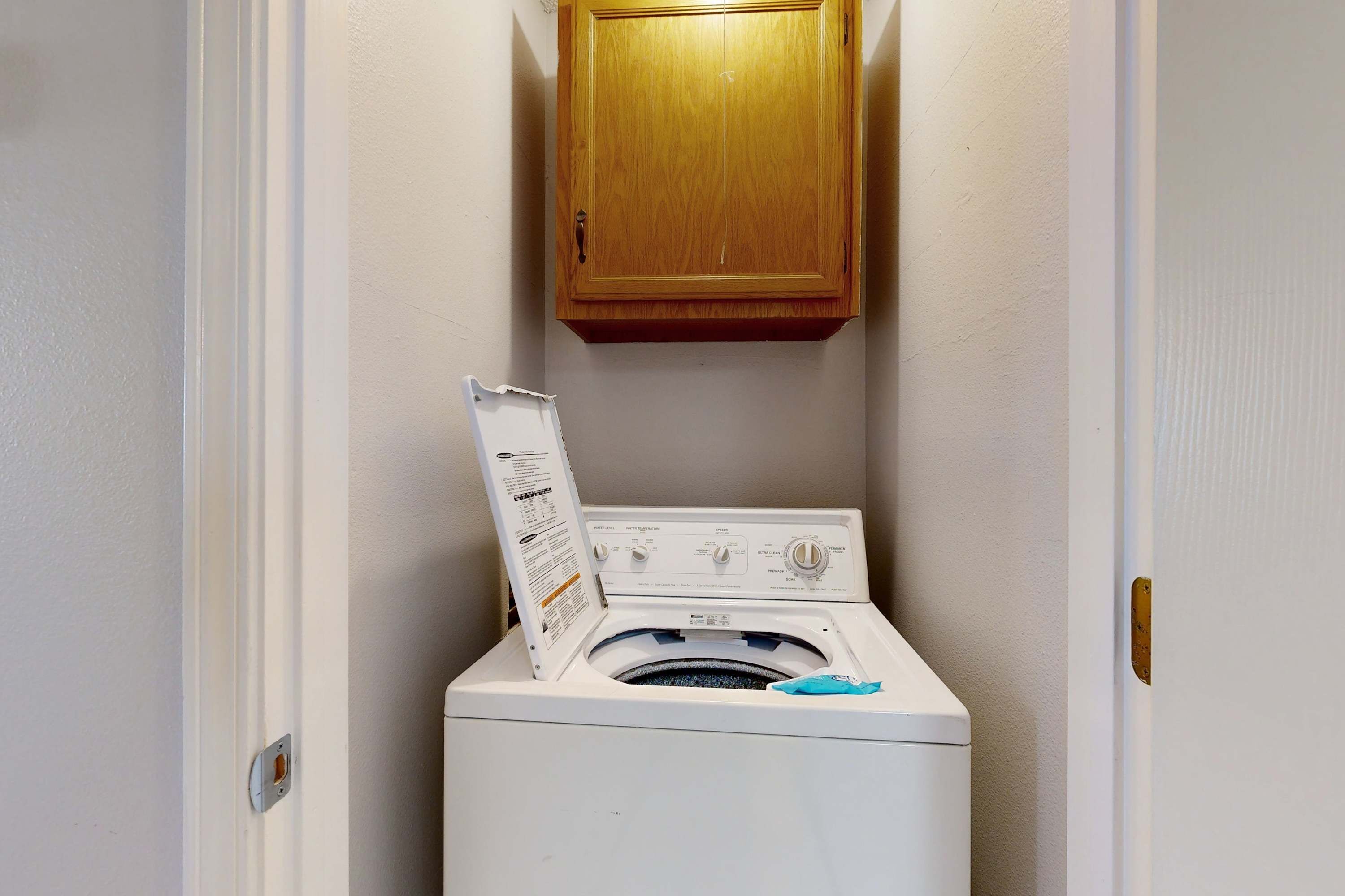 Een kleine wasruimte met een voorlader wasmachine en droger, een houten kast erboven en een deur aan de linkerkant.