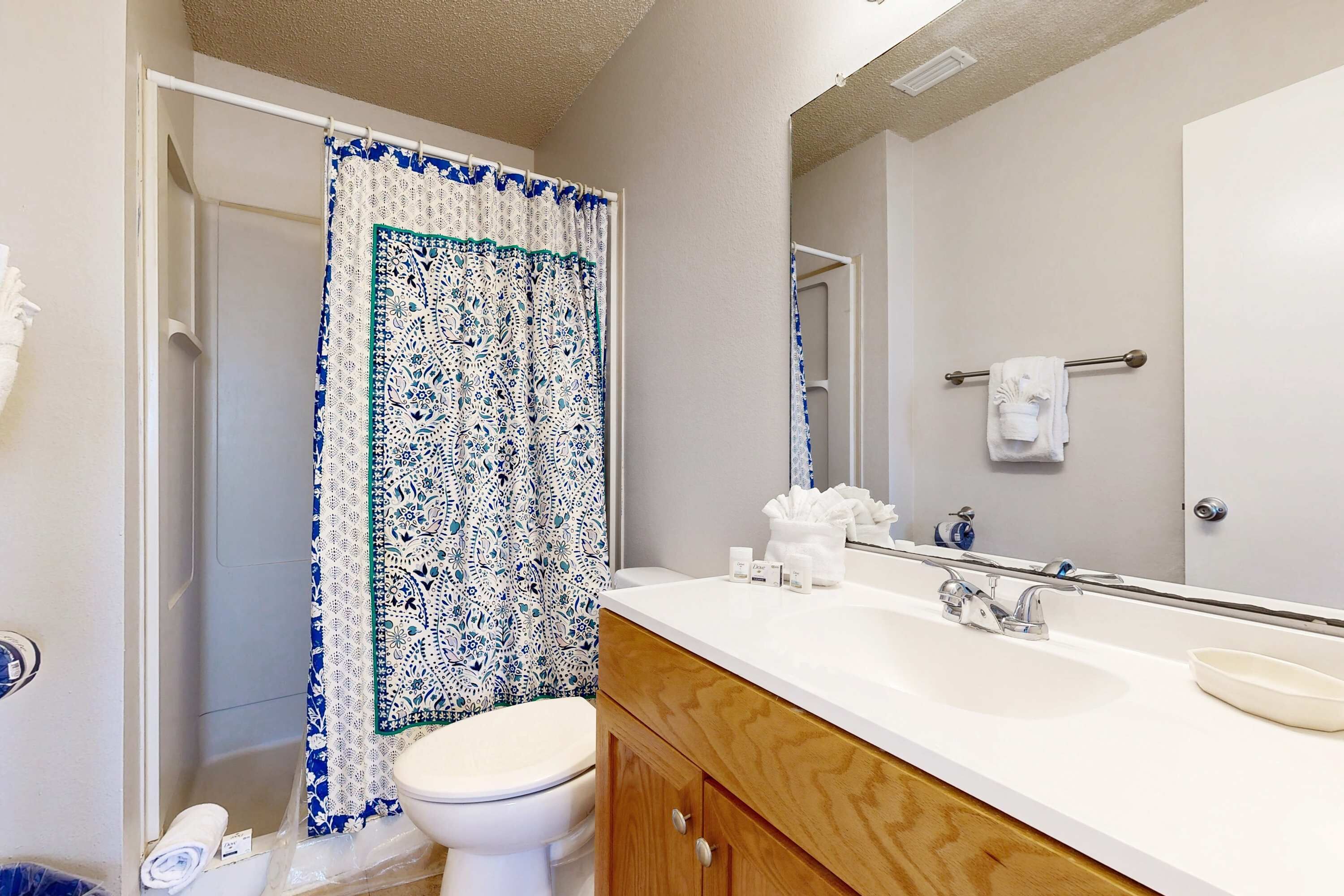 A bathroom with a shower curtain, toilet, sink, and mirror.