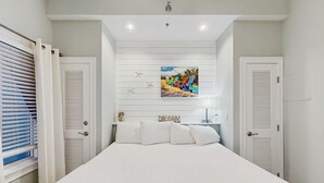 Ein Schlafzimmer mit einem großen Bett, weißen Wänden, einer Deckenleuchte, einem Gemälde und zwei Türen.